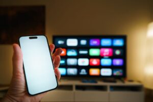 Smartphone em foco com Smart TV exibindo aplicativos na sala